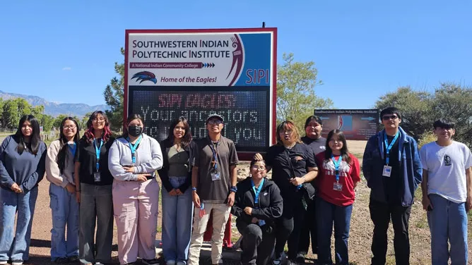 Students taking a photo in front of the Southwestern Indian Polytechnic Institute school signs.