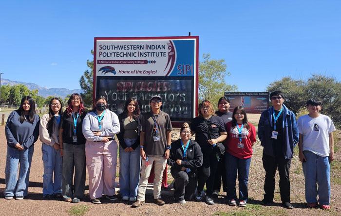 Students taking a photo in front of the Southwestern Indian Polytechnic Institute school signs.